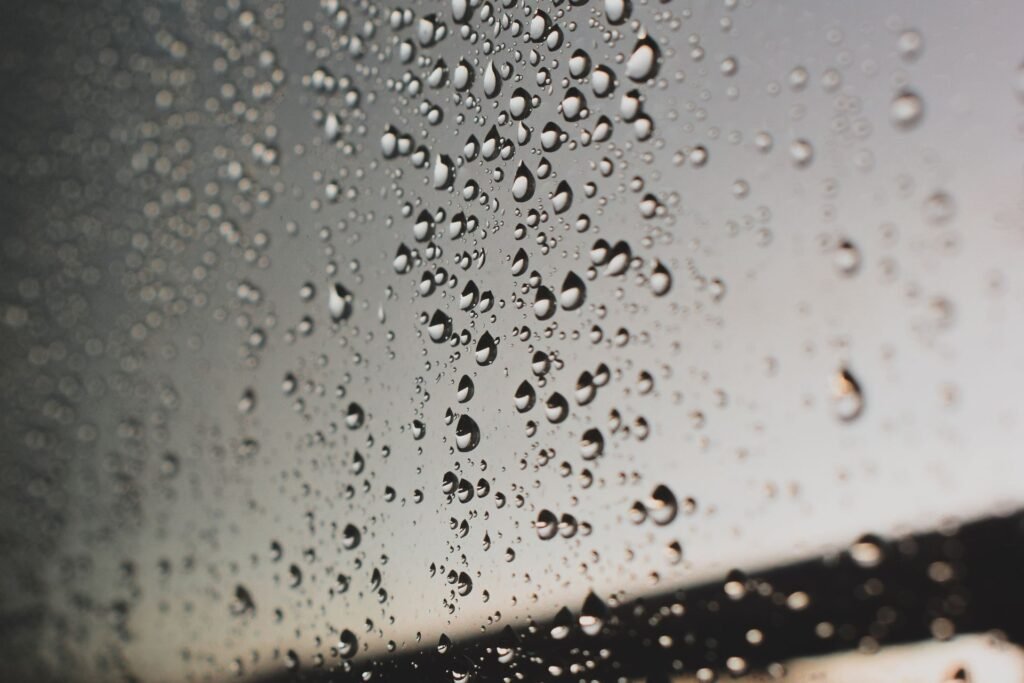 Raindrops running down a window pane against soft grey monsoon light