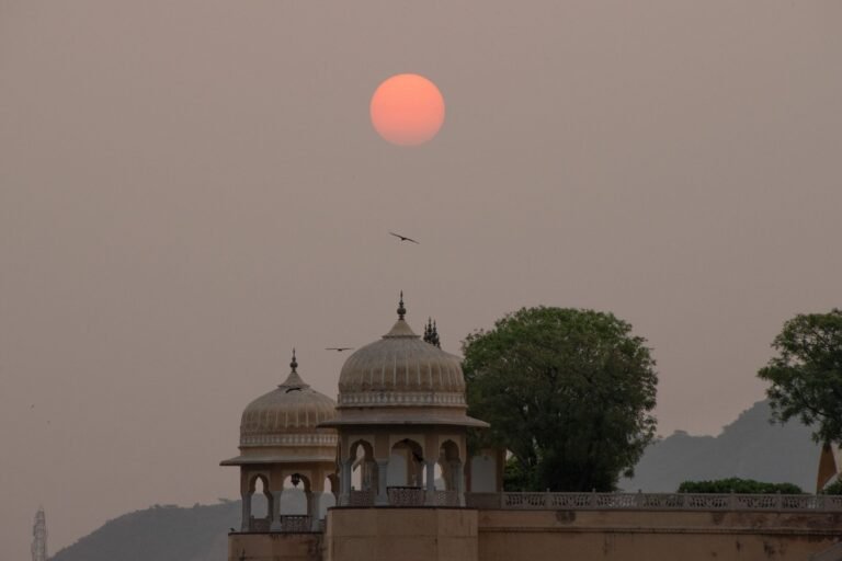 Domes of a Mughal-era building in Jaipur silhouetted against a hazy, sun-bleached sky during peak Indian summer heat.