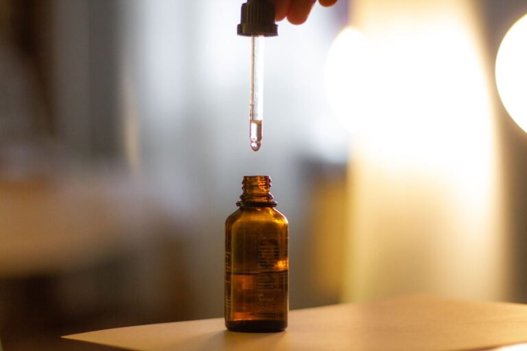 A serum dropper poised above an amber glass bottle in warm natural light